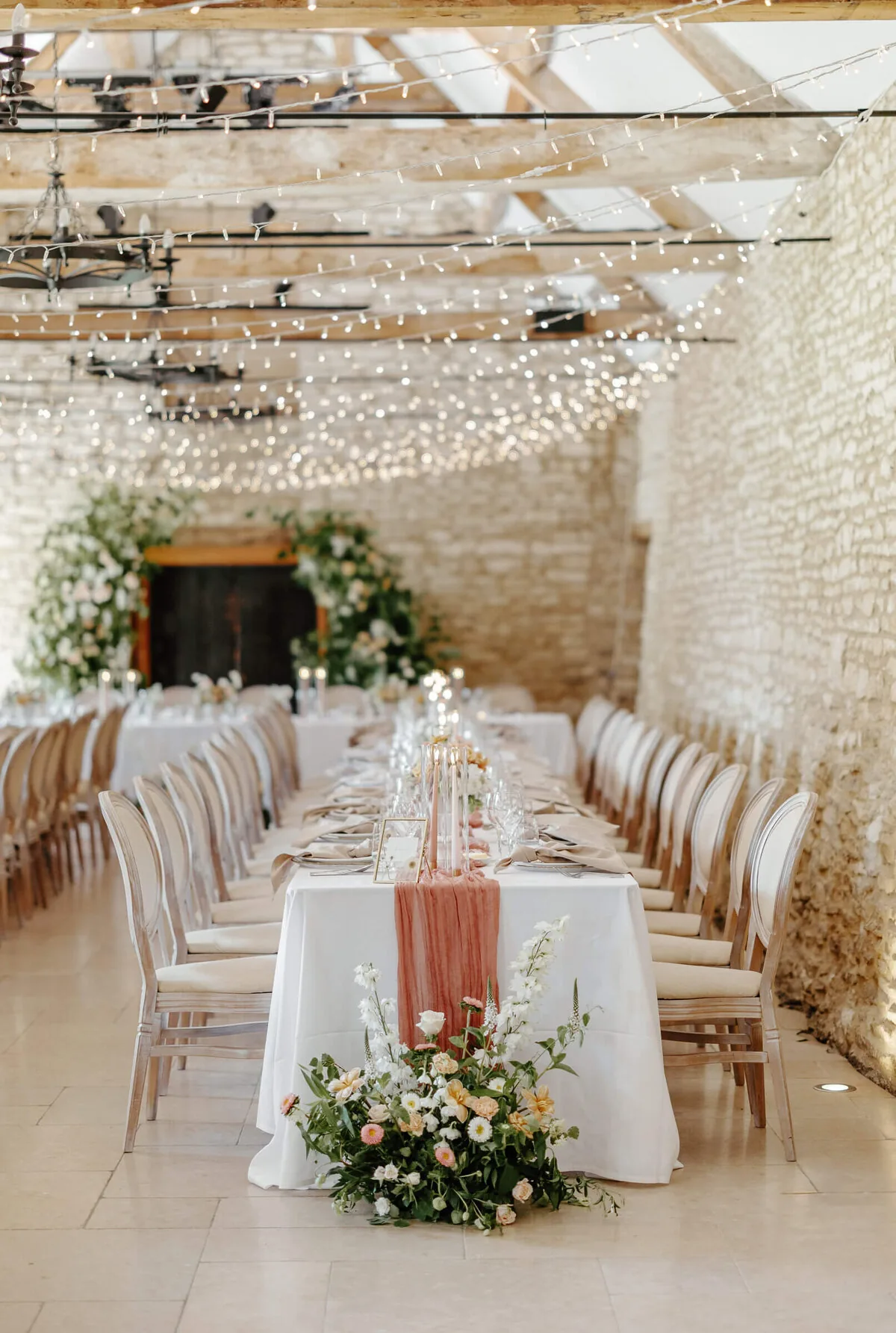 The barn at Caswell House dressed for a wedding reception, long tables with florals and fairy lights
